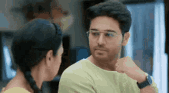a man and a woman are looking at each other in a room . the man is wearing glasses .