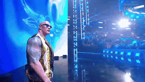 a man wearing sunglasses stands on a stage in front of a large screen that says smackdown