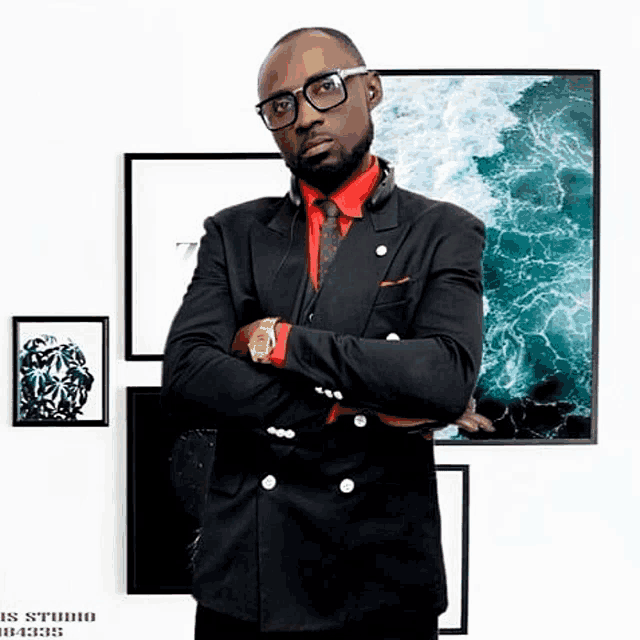 a man in a black suit and red shirt is standing in front of a wall with pictures on it and the word studio on the bottom right