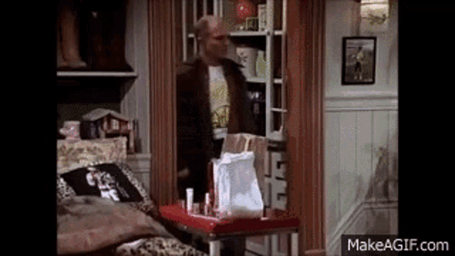 a man is standing next to a table with a bag of food on it in a living room .