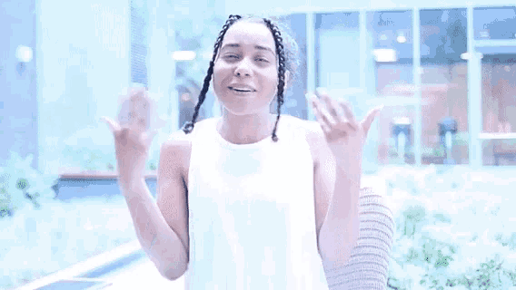 a woman wearing a white tank top is smiling and holding her hands to her chest .