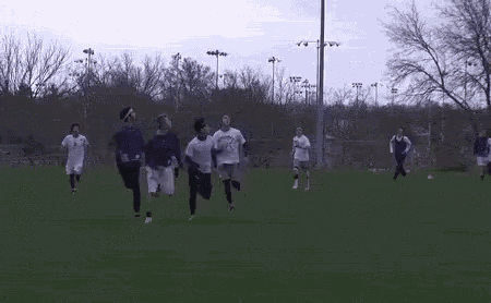 a group of soccer players are running on a field with trees in the background .