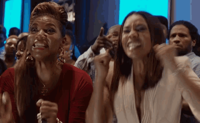two women are sitting in a crowd with their arms in the air and making funny faces .