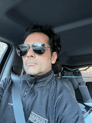 a man wearing sunglasses is sitting in a car with a shirt that says " altitude " on it