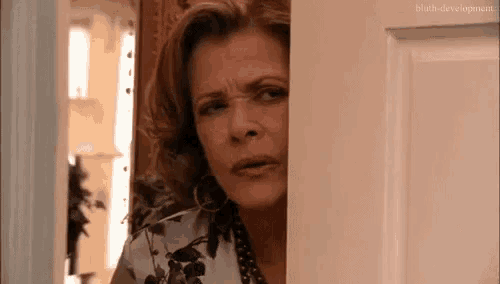 a woman is peeking out from behind a door and making a face .