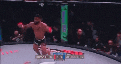 a man is kneeling down in a boxing ring while a crowd watches .