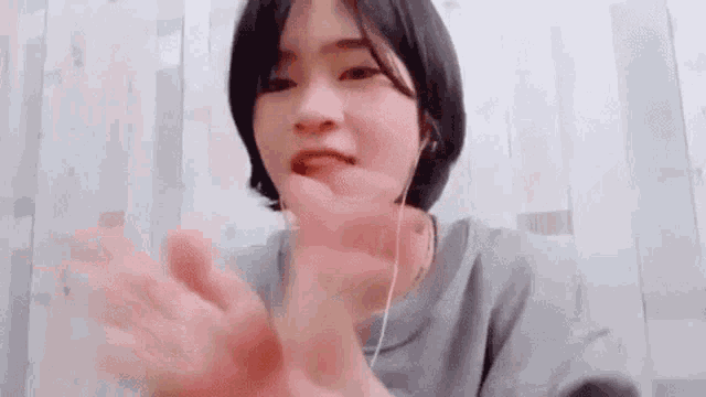 a woman wearing headphones and a gray sweater is making a hand gesture .