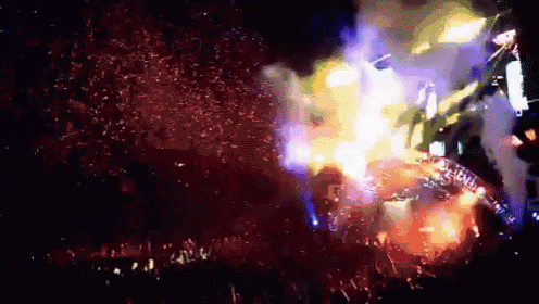 a crowd of people at a concert with a huge explosion in the background