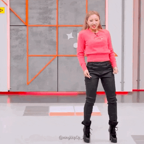 a woman in a pink sweater and black pants is standing on a floor .
