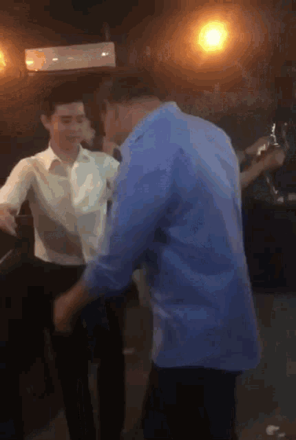a man in a blue shirt is dancing with another man in a white shirt in a dark room