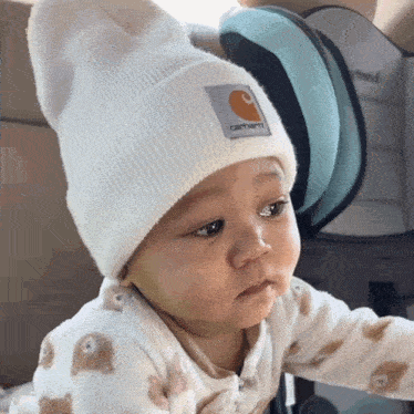 a baby wearing a white carhartt beanie is looking at the camera