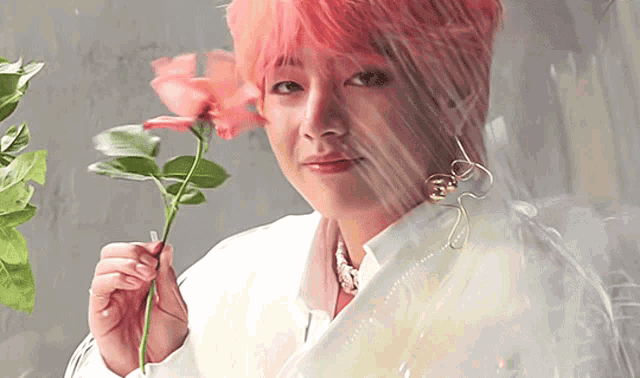 a man with pink hair is holding a rose in his hand