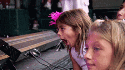 two little girls are making funny faces while sitting on a stage at a concert .