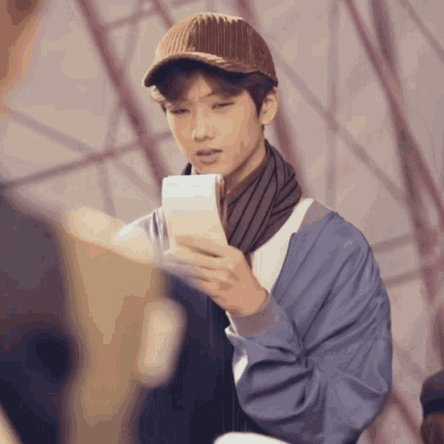 a man wearing a hat and scarf holds a piece of paper in his hand