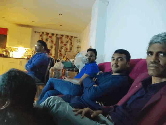 a group of men are sitting on a couch and one of them is wearing a blue shirt