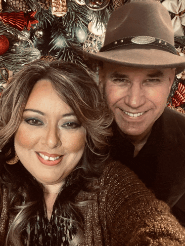 a man wearing a hat and a woman smiling in front of a christmas tree