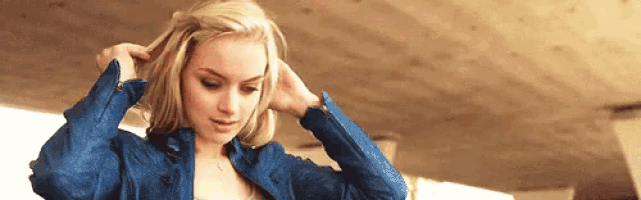 a woman in a blue jacket is holding her hair in a braid .