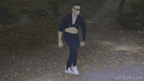 a man wearing sunglasses and a crop top is standing on a road with a gifrun.com logo in the corner