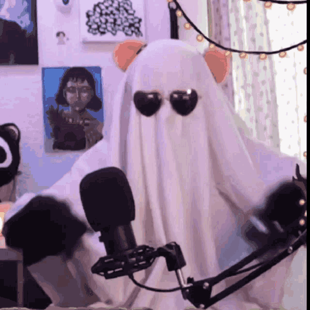 a person in a ghost costume is wearing sunglasses and sitting in front of a microphone .