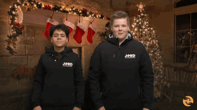 two boys wearing jackets that say jord on them are dancing in front of a christmas tree