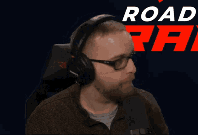 a man wearing headphones giving a thumbs up in front of a sign that says road rat