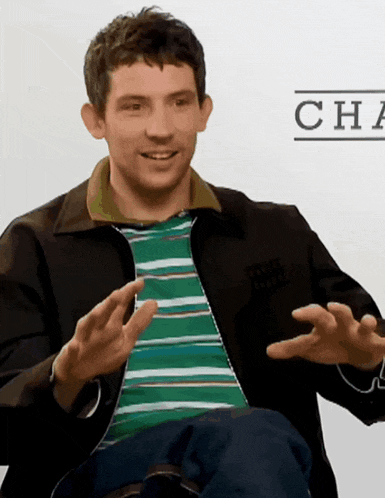a man wearing a green and white striped shirt and a black jacket has his hands out
