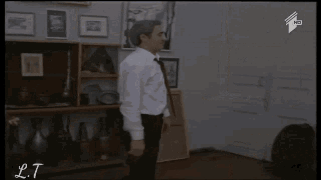 a man in a white shirt is walking in a room with a shelf full of vases and paintings on the wall