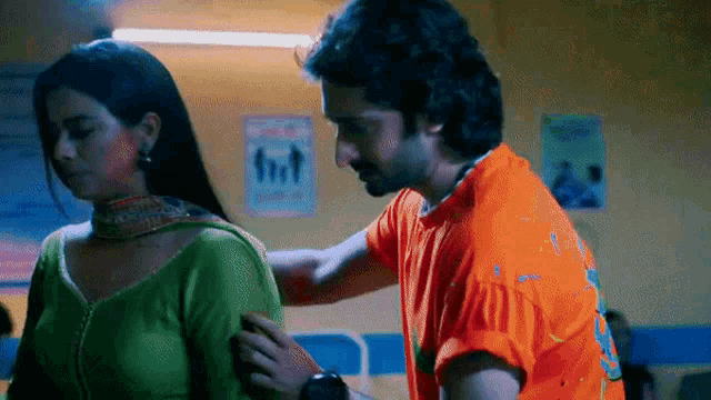 a man in an orange shirt is touching a woman 's back .