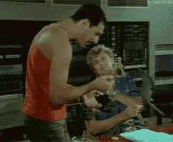 a man in an orange tank top is standing next to another man in a blue shirt .