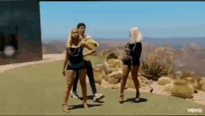 a man and two women are dancing on a grassy hillside in a video for vevo