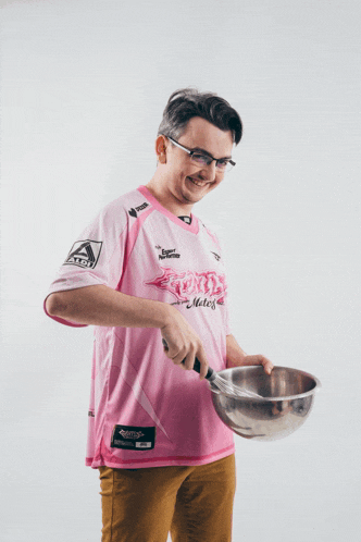 a man in a pink shirt holding a bowl and a whisk