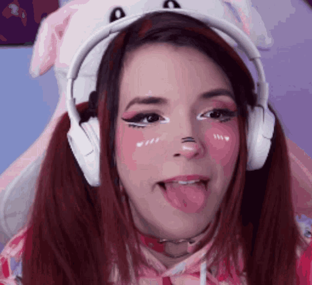 a girl wearing headphones and a bunny hat sticks out her tongue