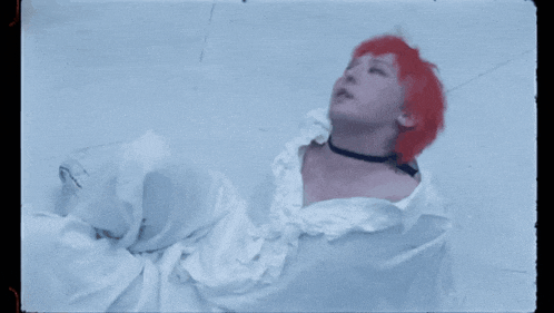 a woman with red hair is laying on the floor in a white dress