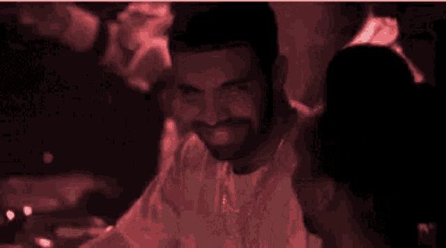 a man with a beard and a necklace smiles in a dark room