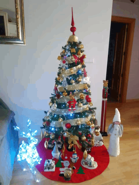 a christmas tree in a living room with decorations and a red skirt that says ' christmas ' on it