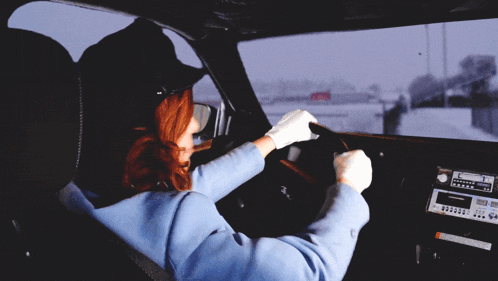 a woman in a blue jacket and black hat is sitting in a car with a radio on the dashboard