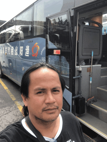 a man stands in front of a blue bus with chinese characters on the side