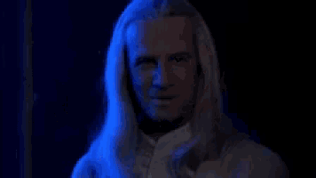 a man with long white hair is laughing in a dark room with the words ha ha ha behind him .