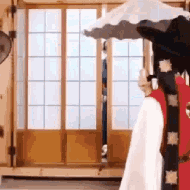 a woman in a white dress is standing under an umbrella in front of a window in a room .