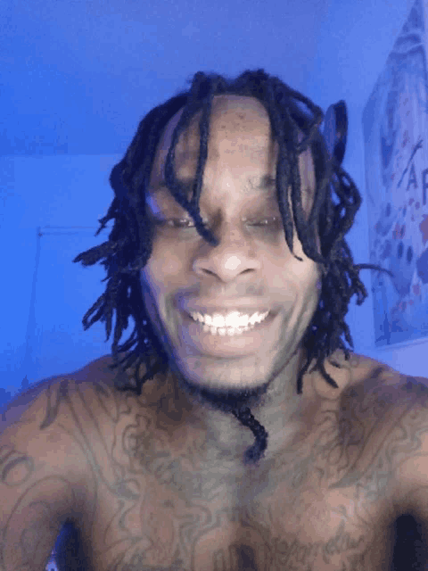 a shirtless man with dreadlocks and tattoos on his chest smiles