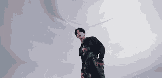 a young man in a black sweater and black leather pants is dancing in front of a white wall .