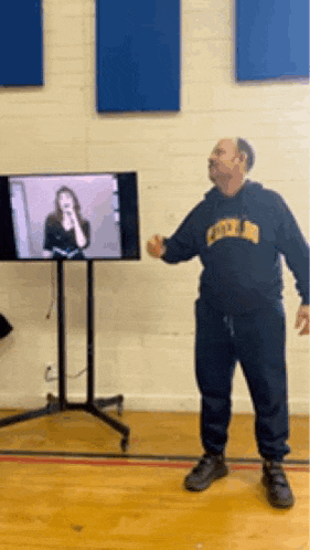 a man wearing a sweatshirt that says duke is standing in front of a television .