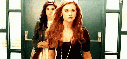 two women are standing next to each other in front of a door and looking at the camera .