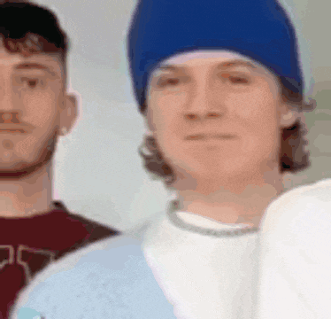 a man wearing a blue beanie is standing next to another man wearing a white shirt .