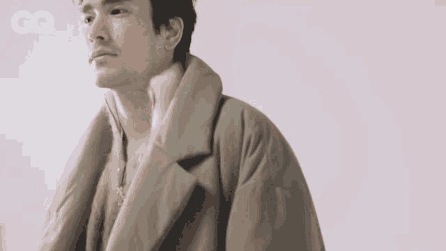 a man wearing a coat with a gq logo on the bottom