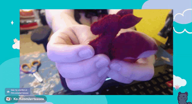 a person is holding a stuffed animal in front of a keyboard and a screen that says ko-fi.com/artoasea