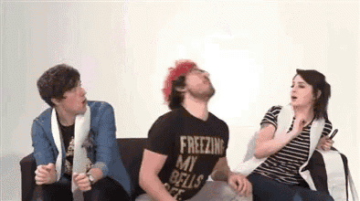 a group of people are sitting on a couch and one of them is wearing a shirt that says freezing my bells .