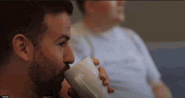 a man drinking from a white mug with the word plus written on the bottom right corner