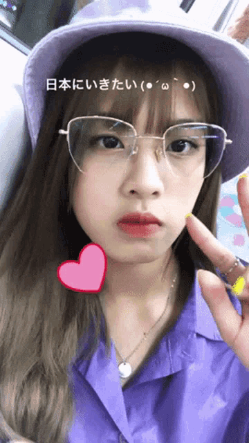 a girl wearing glasses and a purple shirt is giving a peace sign in japanese