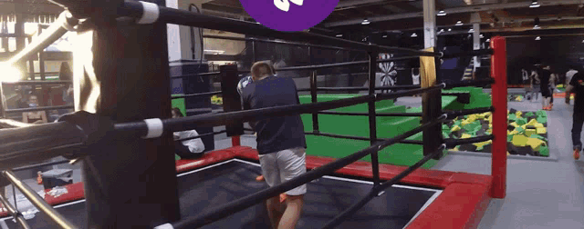 a man in a blue shirt is standing in a boxing ring with a purple circle with the letter s on it
